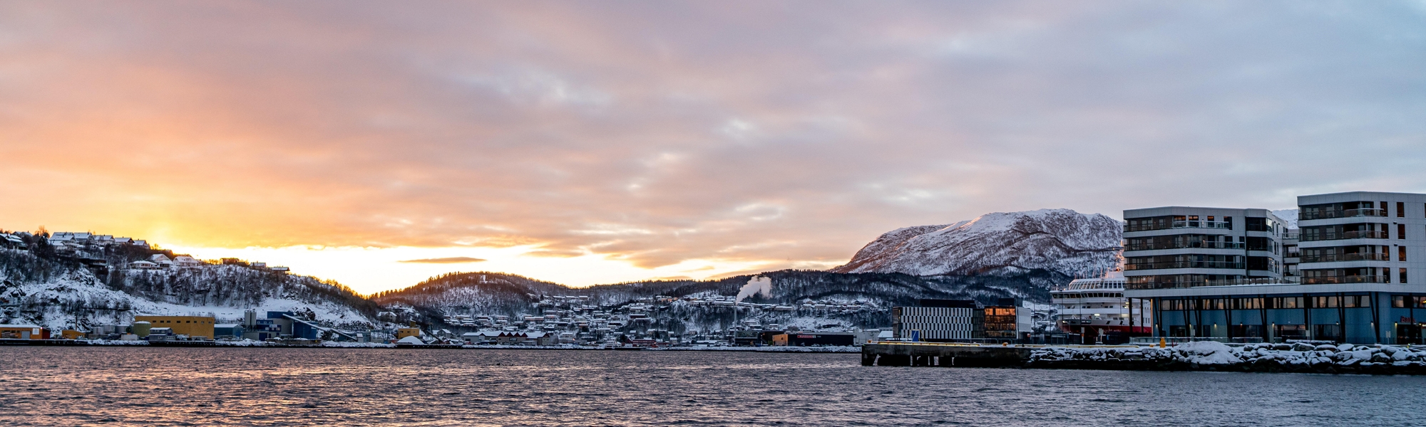 The Equinor office in Harstad, seen from the seaside. The picture is taken in winter just before sunset, with a snowy landscape in the background