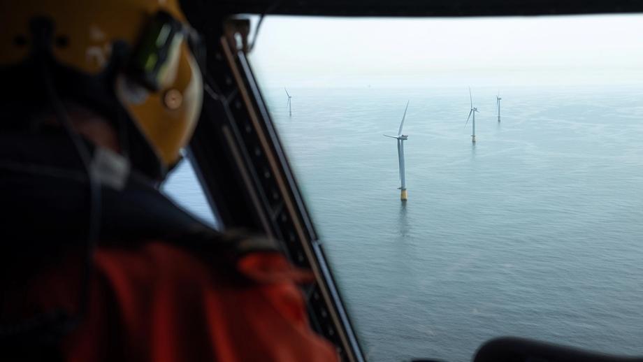 A view of the Hywind Tampen wind farm from a helicopter is shown, with the back of a person wearing a helmet faintly visible in the foreground.
