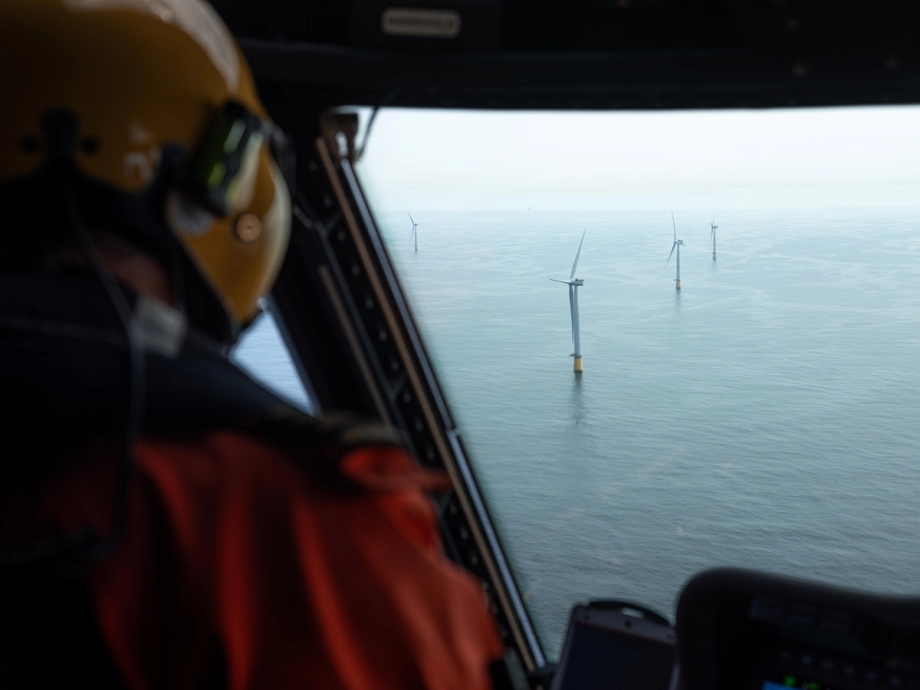 A view of the Hywind Tampen wind farm from a helicopter is shown, with the back of a person wearing a helmet faintly visible in the foreground.