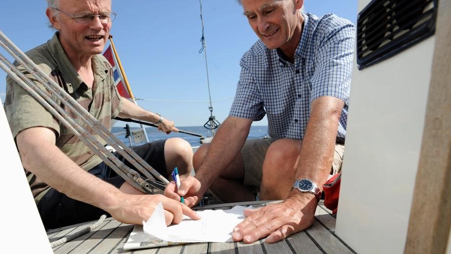 To menn på dekket i en båt med penn og papir