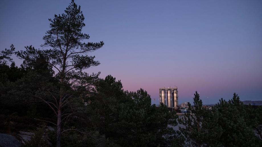 The Northern Lights CCS plant can be seen in the background, with forest in the foreground, at dusk. 